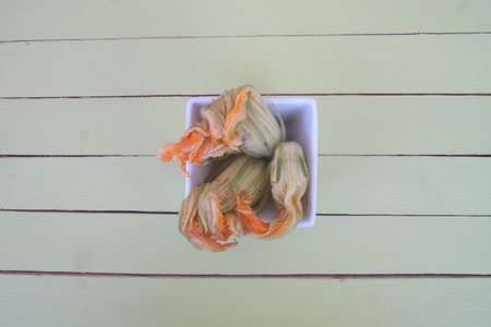 pumpkin flowers in white bowl on a green wooden table seen from aboveの写真素材