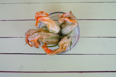pumpkin flowers in transparent bowl on a green wooden table seen from aboveの写真素材