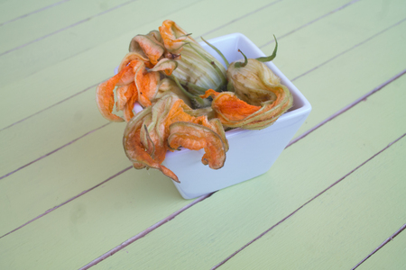 Pumpkin flowers in white bowl on a green wooden table seen close upの写真素材