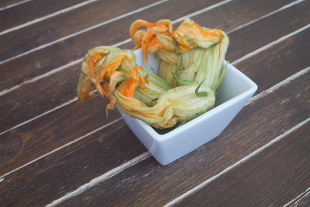 pumpkin flowers in white bowl on a wooden table seen close upの写真素材