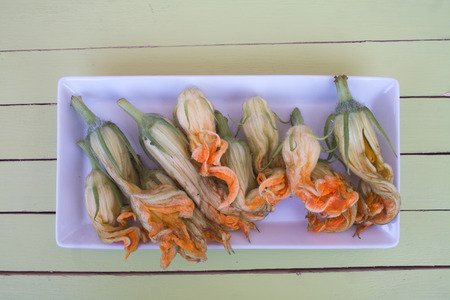 pumpkin flowers on white tray on a green wooden table seen from aboveの写真素材