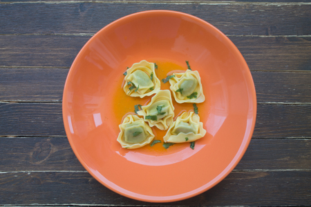 tortellini in broth on orange plate on a wooden table viewed from aboveの写真素材