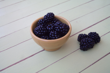 blackberries on yellow bowl on a green wooden table seen close upの写真素材