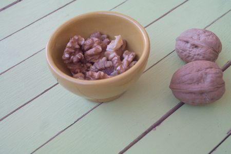 walnuts in a yellow bowl on a green wooden table seen close upの写真素材