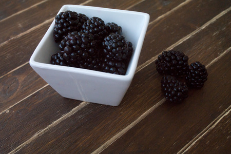 blackberries on white bowl on a wooden table seen close upの写真素材