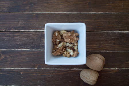 walnuts in a white bowl on a wooden table seen from aboveの写真素材