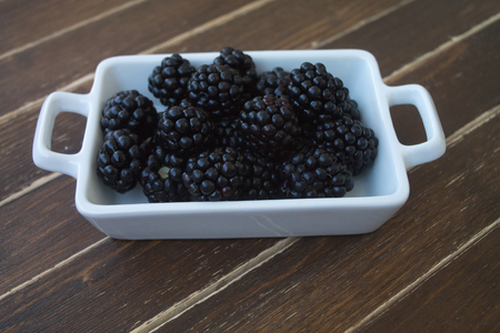 blackberries on white tray on a wooden table seen close upの写真素材