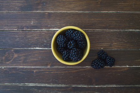 blackberries on yellow bowl on a wooden table seen from aboveの写真素材