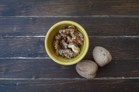 walnuts in a yellow bowl on a wooden table seen from aboveの写真素材