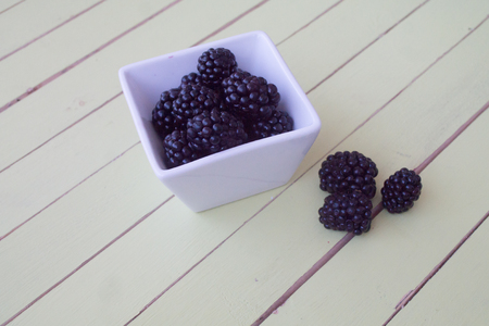 blackberries on white bowl on a green wooden table seen close upの写真素材
