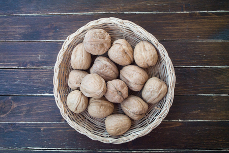 walnuts inside a wicker basket on a wooden table seen from aboveの写真素材