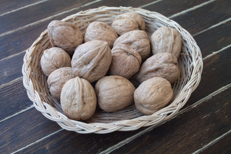walnuts inside a wicker basket on a wooden table seen close upの写真素材