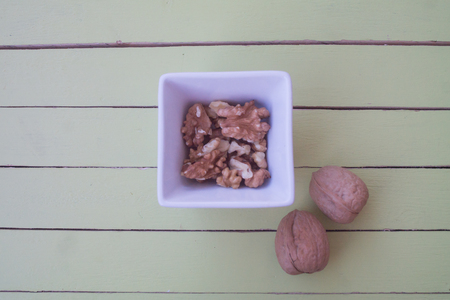 walnuts in a white bowl on a green wooden table seen from aboveの写真素材