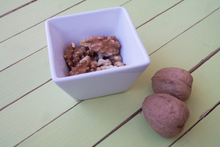 walnuts in a white bowl on a green wooden table seen close upの写真素材