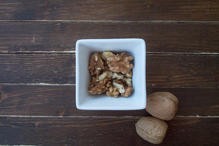 walnuts in a white bowl on a wooden table seen from aboveの写真素材