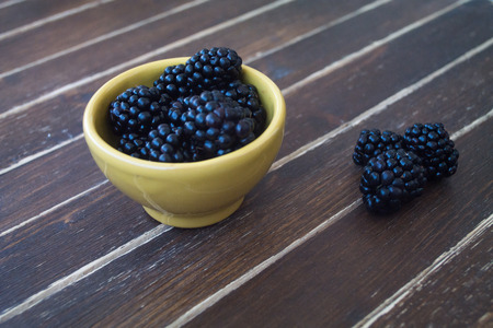blackberries on yellow bowl on a wooden table seen close upの写真素材