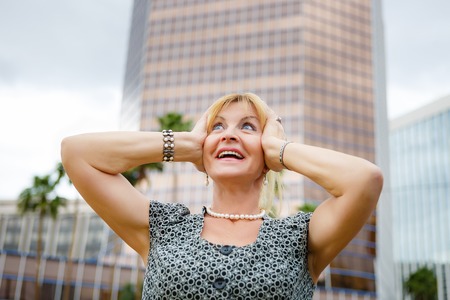 Happy old senior blonde woman 6065 years with white teeth on city backgroundの写真素材