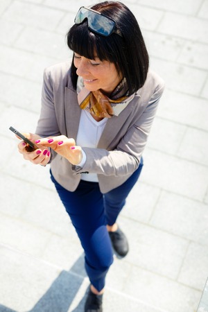 Happy, cheerful, brunette woman, excited by what she sees on cell phone, Facial expression, reaction. Business woman sending text message from her mobileの写真素材
