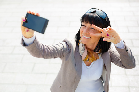 Stylish woman 30 years, smiling pretty woman taking pictures selfie her phone and have fun, dressed in suit, sunny day, city street, soft light series, Positive emotion, facial expression, spring moodの写真素材