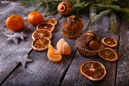 Xmas or new year composition with holiday decoration - Homemade christmas cupcakes, sliced dried oranges on wooden background with spruce twigs and christmas toy. Christmas card. Space for textの写真素材