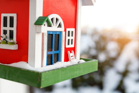 Wooden bird house of red color hanging outdoors in winter covered with snowの写真素材