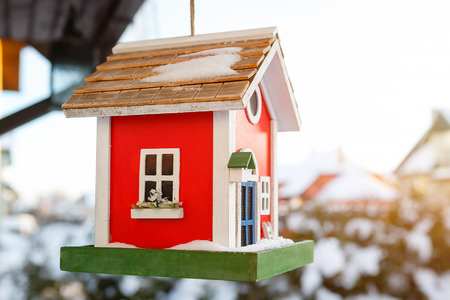 Wooden bird house of red color hanging outdoors in winter covered with snowの写真素材