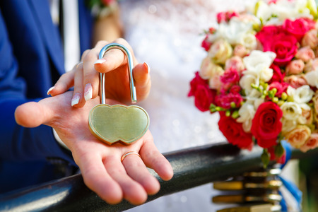 The decorative lock in hands of newlyweds, Space for text on lock. Wedding Bouquet on backgroundの写真素材
