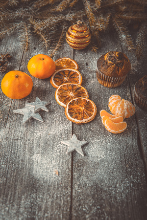 Xmas or new year composition with holiday decoration - Homemade christmas cupcakes, sliced dried oranges and mandarin on wooden background with spruce twigs and christmas toy. Christmas card. Space for textの写真素材