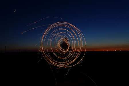spiral of light in the field during sunset with the moon in the sky and the red and blue colors of a...