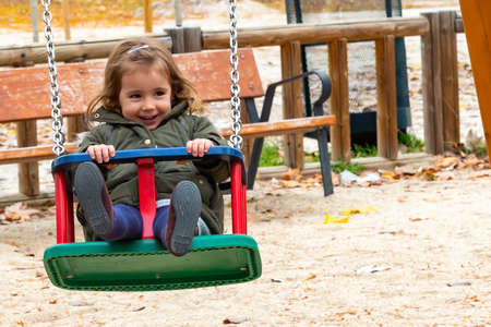Little girl playing on the swings in a park. Kids' games