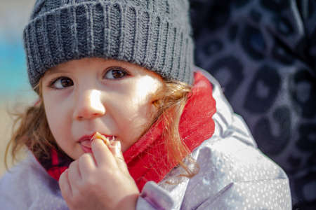 Little girl in a woolen hat and red scarf eating Serrano ham. Children with winter clothes