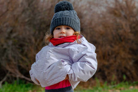 Little girl in a woolen hat and red scarf playing in the field. Little girl with winter clothesの写真素材