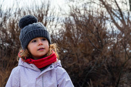 Little girl in a woolen hat and red scarf playing in the field. Little girl with winter clothesの写真素材