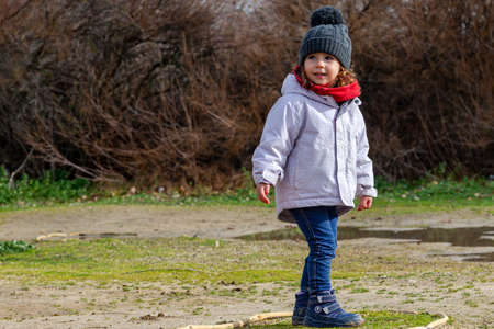 Little girl in a woolen hat and red scarf playing in the field. Little girl with winter clothesの写真素材