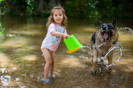Little girl playing with some plastic buckets in the river. Girl with swimsuit and t-shirt. Children's photo in summer.の写真素材