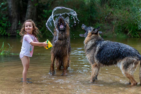 Little girl playing with some plastic buckets in the river. Girl with swimsuit and t-shirt. Children's photo in summer.の写真素材