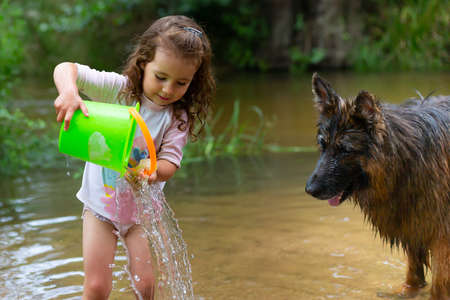 Little girl playing with some plastic buckets in the river. Girl with swimsuit and t-shirt. Children's photo in summer.の写真素材
