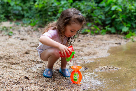 Little girl playing with some plastic buckets in the river. Girl with swimsuit and t-shirt. Children's photo in summer.の写真素材