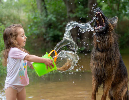 Little girl playing with some plastic buckets in the river. Girl with swimsuit and t-shirt. Children's photo in summer.の写真素材