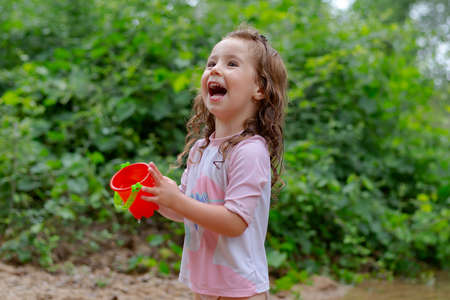Little girl playing with some plastic buckets in the river. Girl with swimsuit and t-shirt. Children's photo in summer.の写真素材