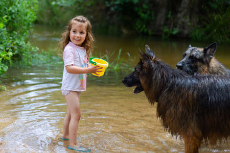 Little girl playing with some plastic buckets in the river. Girl with swimsuit and t-shirt. Children's photo in summer.の写真素材