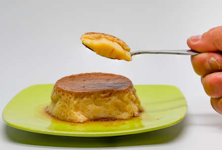 Egg custard on a green plate and a spoon with a piece of custard held in one hand. Sugar desserts. Sugary foods. Side photo.の写真素材