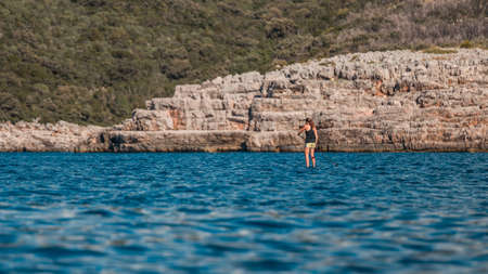 Young athletic woman paddling on a SUP stand up paddle board on a warm summer day overlooking the cliffsの写真素材