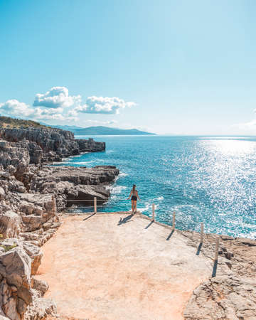 Back view: Beautiful young girl stands on a cliff with a fabulous view of the sea and blue water of Montenegro. Aerial view.の写真素材