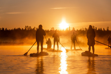 Silhouette of group of people doing SUP stand up paddle boarding at sunrise in lake. Early summer morning activityの写真素材