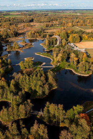 Aerial perspective of an observation tower surrounded by vibrant autumn foliage, interconnected lakes, and lush forests with winding pathways and bridges.の写真素材