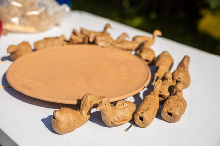 A collection of unpainted clay bird figures arranged on a flat disc, set on a white table with a blurred green background suggesting a garden environment.の写真素材