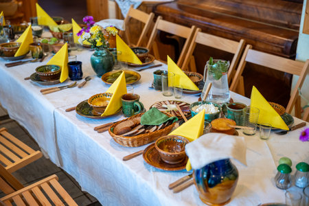 A dining table set with ceramic dishes, yellow napkins, and a floral centerpiece. Wooden chairs surround the table, with a piano in the background.の写真素材