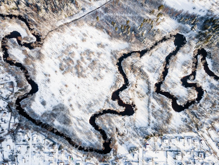 Aerial view on winter river streaming through the field with the tree on it. Everything is covered with snow.の写真素材