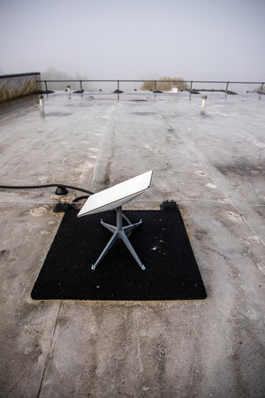 A dish sits on a flat rooftop with light frost, surrounded by fog. A railing encircles the roof, indicating safety in a remote location.の写真素材